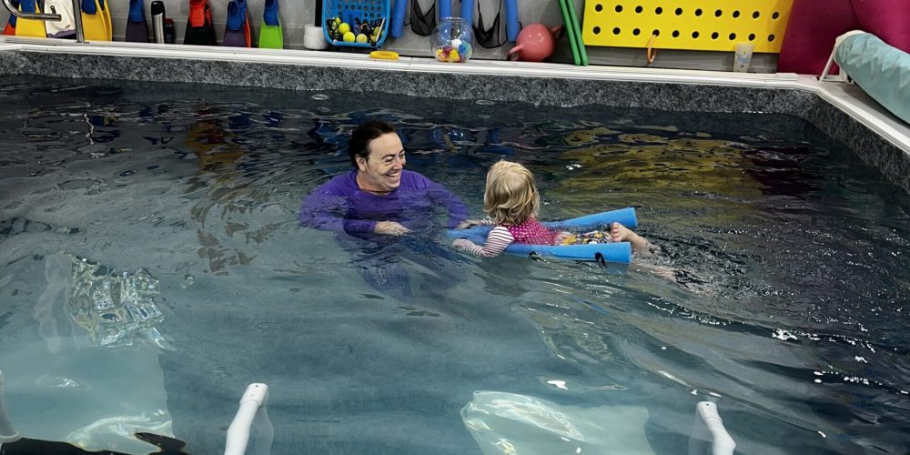 A picture of a young girl swimmer from Thistledown Swim Academy riding on a bent pool noodle boat